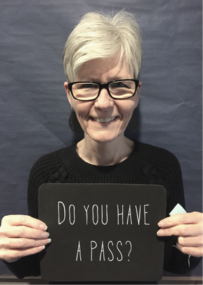 woman with white hair, black glasses, black shirt, and sign with text: Do you have a pass?